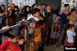 Children watch as women queue to receive free clothes at a makeshift camp for refugees and migrants at the Greek-Macedonian border near the village of Idomeni, Greece, May 12, 2016.