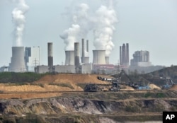 FILE - Machines dig for brown coal in front of a smoking power plant near the city of Grevenbroich in Germany.