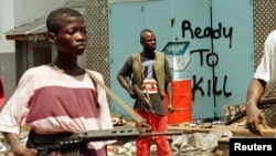 FILE - Street fighters with ULIMO-J walk past graffiti in the Liberian capital of Monrovia in this May 1996 photo.