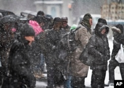 FILE - Pedestrians gather at a bus stop during snowfall along Lexington Avenue, Jan. 21, 2014 in New York.
