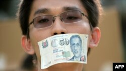 FILE - A protester covers his mouth with a Singapore fifty-dollar note during a rally at a free-speech park called Speakers' Corner in Singapore, June 8, 2013.