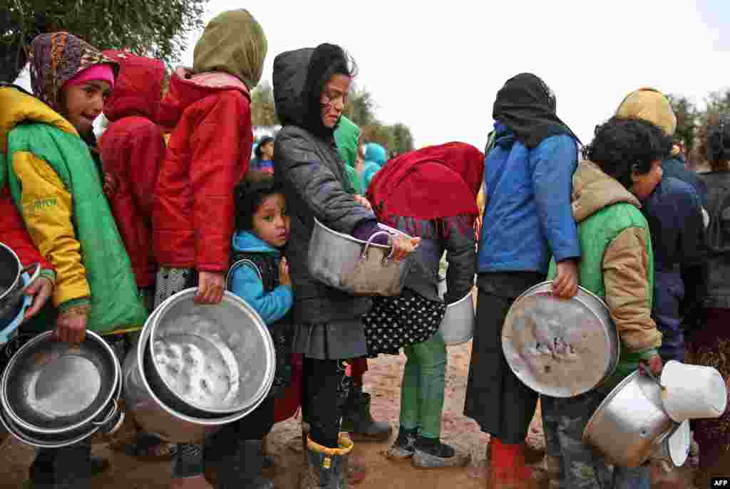 Syrian children queue to receive food distributed by humanitarian aid workers at a makeshift camp for displaced people, near the village of Yazi Bagh, about six kilometers from the Bab al-Salamah border crossing between Syria and Turkey in the north of Aleppo province.