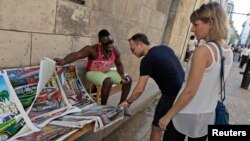 FILE - A vendor shows tourists prints for sale in Old Havana, Cuba, Dec.18, 2014. 