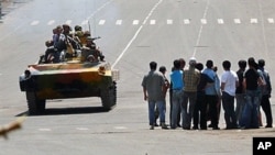 Kyrgyz soldiers on an armored vehicle drive past a group of people in Osh on 11 Jun 2010