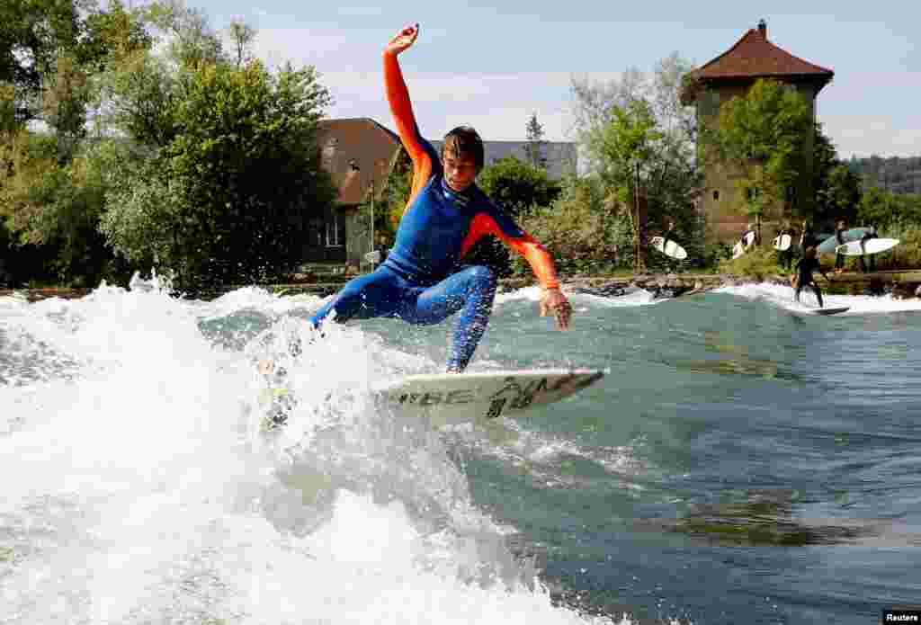 A man surfs on a wave on the Reuss river during sunny weather in the town of Bremgarten, Switzerland.