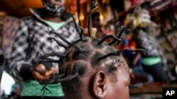 In this Sunday, May 3, 2020 file photo, Gettrueth Ambio, 12, has her hair styled in the shape of the new coronavirus, at the Mama Brayo Beauty Salon in the Kibera slum, or informal settlement, of Nairobi, Kenya. (AP Photo/Brian Inganga, File)