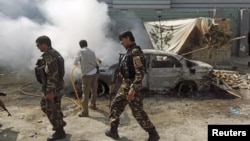 Afghan security forces walk past a burning car after a group of Taliban insurgents stormed a compound used by Afghanistan's intelligence agency in Kabul, Afghanistan, July 7, 2015.