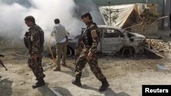 FILE - Afghan security forces walk past a burning car after a group of Taliban insurgents stormed a compound used by Afghanistan's intelligence agency in Kabul, Afghanistan, July 7, 2015.