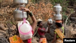 FILE - A woman helps another in carrying metal pitchers filled with water from a well outside Denganmal village, Maharashtra, India, April 20, 2015.