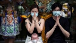 Chinese tourists wearing protective masks pray at the Erawan Shrine in Bangkok, Thailand