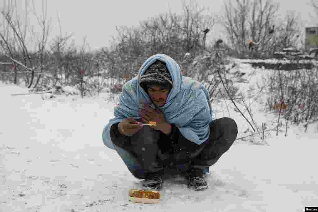 Seorang migran menikmati makanan gratis selama turunnya salju di luar gudang tradisional yang telah ditinggalkan di Beograd, Serbia.