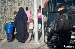 FILE - A Spanish civil guard holds his gun as women and children walk up a street during an operation to detain two men suspected of using social media to recruit people to violent groups like the Islamic State.