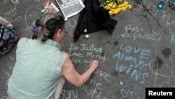 A woman writes a message on the street commemorating the victims at the scene of a car attack on a group of counter-protesters during the a white supremascist rally in Charlottesville, Virginia, Aug. 14, 2017. 
