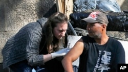 Medical outreach worker Ella Cantrell, left, gives a shot to Wilson Maldonado in New York, Oct. 4, 2017. The nation's most populous city also has the nation's largest homeless population, with 75,000, and like other high-rent cities, it has not been able to move the dispossessed to permanent housing nearly as fast as people are becoming homeless.