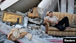 Seorang warga Palestina duduk di sofa di tengah reruntuhan rumahnya yang hancur di Gaza karena serangan Israel, 2014.