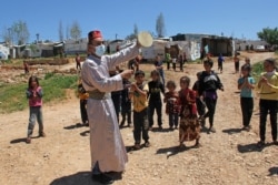 Anak-anak berkumpul di sekitar aktor tunggal yang tampil untuk menghibur anak-anak di kamp pengungsi Suriah, kota selatan Lebanon, Ebel al-Saqi di bulan Ramadan, 23 April 2021. (Foto: Ali DIA / AFP)