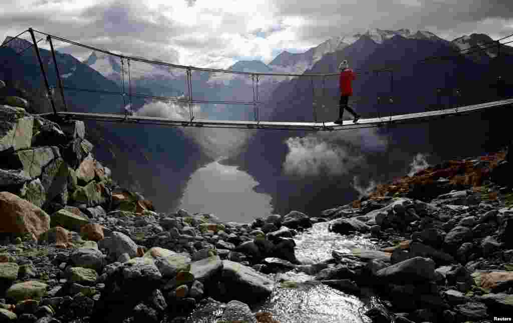 A woman walks on a swing bridge on a sunny autumn day near the alpine village of Ginzling, Austria.