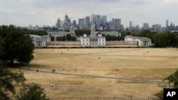 FILE - A view shows parched grass from the lack of rain in Greenwich Park, backdropped by the Royal Museums Greenwich and the skyscrapers of the Canary Wharf business district, during what has been the driest summer for many years in London, July 24, 2018.