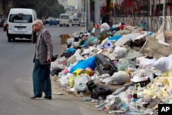A Lebanese man covers his nose from the smell as he passes by a pile of garbage on a street in Beirut, Dec. 17, 2015.