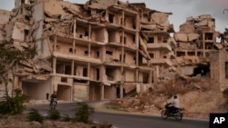 FILE - Motorcycles ride past buildings destroyed during the fighting in the northern town of Ariha, in Idlib province, Syria, Sept. 20, 2018.