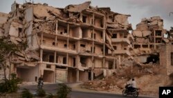In this Sept. 20, 2018 photo, motor cycles ride past buildings destroyed during the fighting in the northern town of Ariha, in Idlib province, Syria. Ariha is one of five main towns in Idlib province and the last place to fall to rebel control in 2015. 