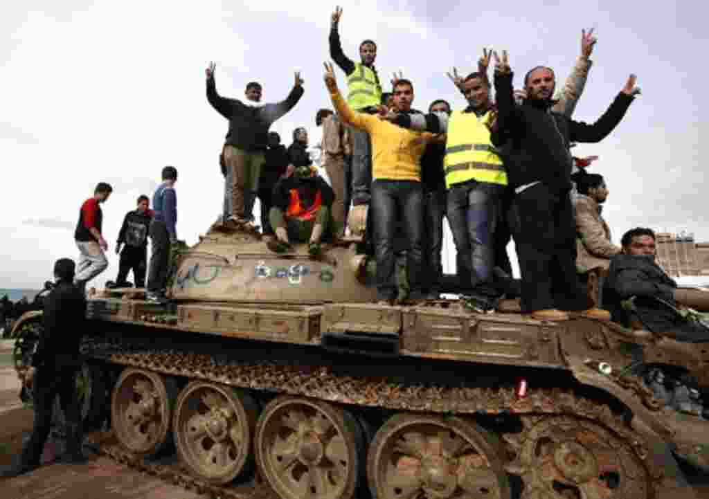 Anti-government protesters make victory signs as they stand on an army tank near a square where people protest in Benghazi city, February 24, 2011