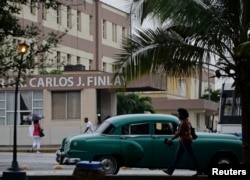 FILE - People walk beside the Carlos J. Finlay Military Hospital where U.S. government contract worker Alan Gross is held prisoner in Havana, March 19, 2013.