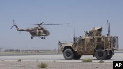 An Afghan National Army helicopter flies in as a U.S. military vehicle passes, at Kandahar Air Base, Afghanistan, Aug. 18, 2015.