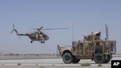 FILE - An Afghan National Army helicopter flies in as a U.S. military vehicle passes, at Kandahar Air Base, Afghanistan, Aug. 18, 2015.