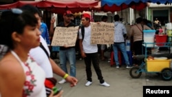 Venezuelan migrants hold signs that read "We are Venezuelans looking for help and a job, God bless you" at the border with Ecuador, in Tumbes, Peru, Aug. 24, 2018. 