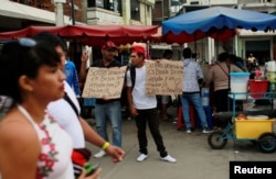 Venezuelan migrants hold signs that read "We are Venezuelans looking for help and a job, God bless you" at the border with Ecuador, in Tumbes, Peru, Aug. 24, 2018.