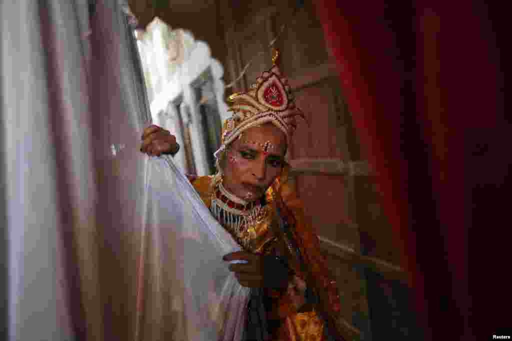 Seorang janda berpakaian sebagai dewi Hindu Radha mengintip dari balik tirai selama perayaan Holi atau festival warna di Vrindavan, negara bagian Uttar Pradesh (24/3). (Reuters/Vivek Prakash)