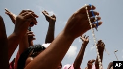 FILE - Women from a Catholic society wave rosary beads as they watch the convoy of Pope Benedict XVI pass on the way to a meeting between the pope and Cameroonian bishops, in Yaounde, March 18, 2009. 