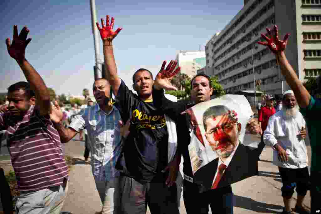 Islamist protesters, one holding a picture of ousted president Mohamed Morsi, hold up blood-stained hands after troops opened fire on a protest in front of the Republican Guard headquarters in Nasr City, Cairo, July 5, 2013