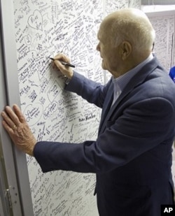 John Glenn signs the wall of the clean room leading into space shuttle Discovery in Orbiter Processing Facility-1 OPF-1 at NASA's Kennedy Space Center in Florida. Glenn is at the space center to mark the 50th anniversary of being the first American astron