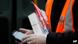 In this March 5, 2020, photo, a Royal Mail employee wears gloves as he hold parcels and the signature handheld as he delivers in London.