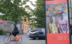 A bicyclist rides next to a billboard, a part of a "Mask Fashion Week" during the coronavirus disease (COVID-19) outbreak in Vilnius, Lithuania May 5, 2020. REUTERS/Andrius Sytas