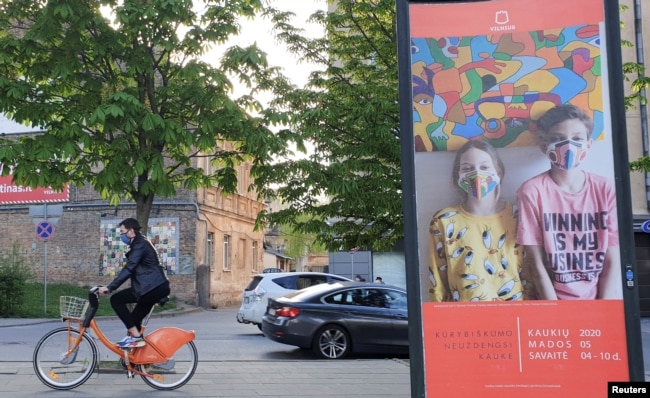 A bicyclist rides next to a billboard, a part of a "Mask Fashion Week" during the coronavirus disease (COVID-19) outbreak in Vilnius, Lithuania May 5, 2020. REUTERS/Andrius Sytas