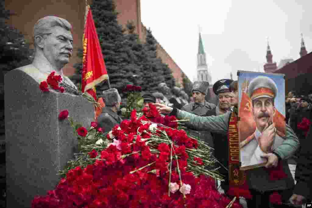 A woman holding a portrait of Stalin places flowers near the monument signifying Joseph Stalin's grave near the Kremlin wall marking the anniversary of Stalin's birth in Moscow's Red Square, Russia.
