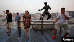 Tourists pose in front of a bronze statue of the late Kung Fu legend Bruce Lee on the waterfront facing Hong Kong island July 12, 2013.