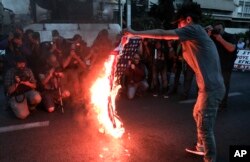 A protester holds a burning U.S. flag during a rally outside the U.S. embassy in Athens, Saturday, April 14, 2018.
