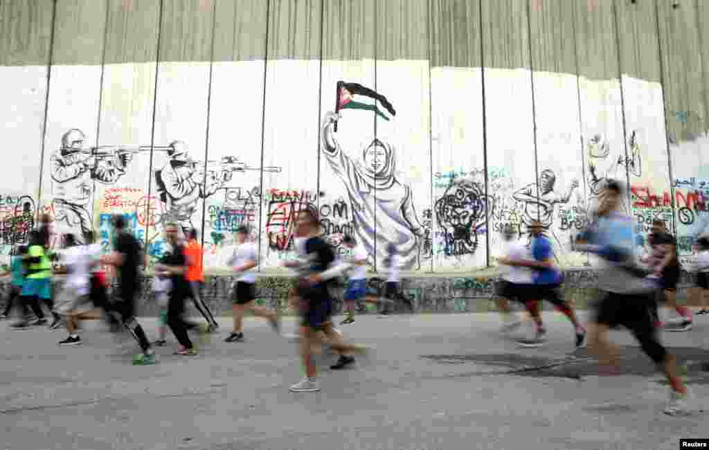 Participants run past the Israeli barrier during the annual Palestine Marathon in the West Bank town of Bethlehem.