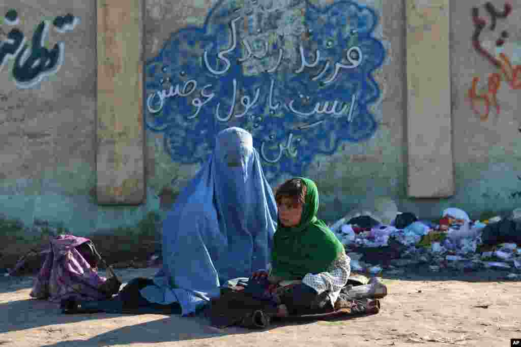 Seorang perempuan Afghanistan duduk bersama seorang anak perempuan mengemis di depan dinding yang bertuliskan &quot;Anak adalah kehidupan, jangan tukar dia dengan uang,&quot; dalam bahasa Persia di Mazar-i Sharif, Kabul utara.