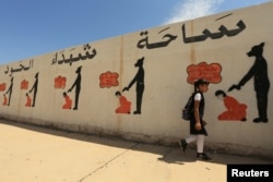 FILE - An Iraqi student walks past a school wall covered with drawings showing how Islamic State militants executed their prisoners in Mosul, Iraq, April 30, 2018.
