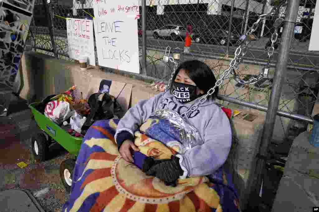 Kia Hirt sits with a chain attached to a fence while protesting outside the Hennepin County Government Center in Minneapolis, Minnesota, where the trial for former police officer Derek Chauvin continues.&nbsp;Chauvin is charged with murder in the death of George Floyd during an arrest last May in Minneapolis.&nbsp;