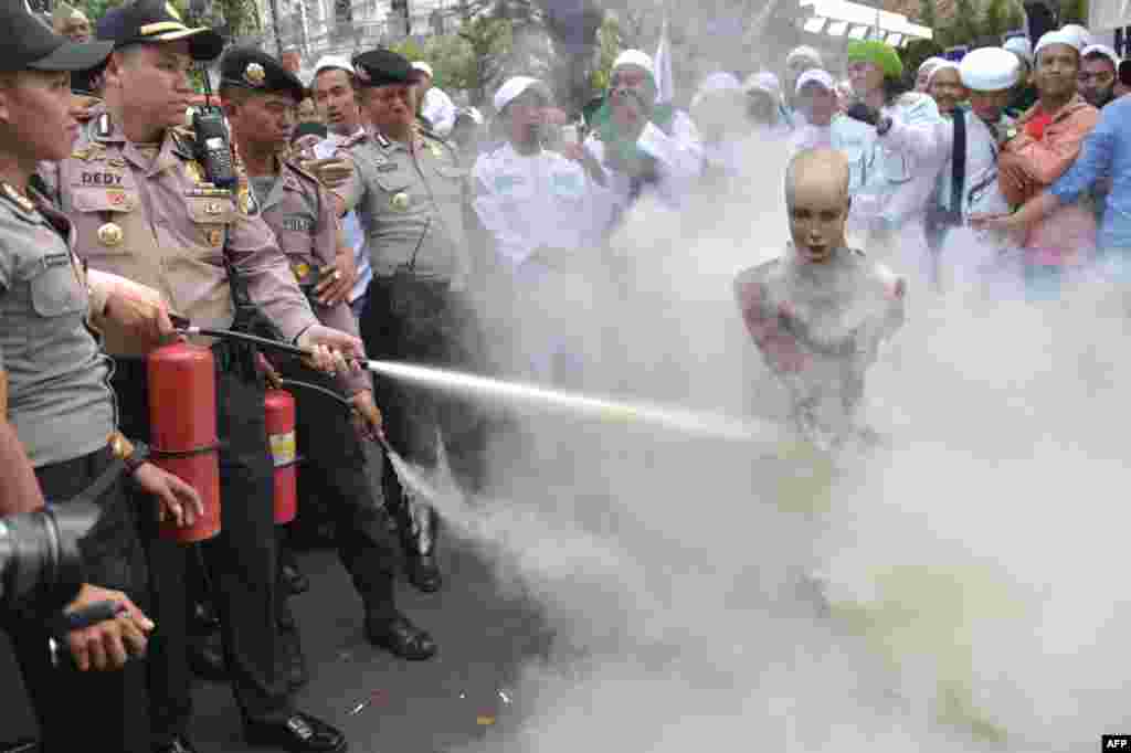 Polisi Indonesia memadamkan patung biksu Budha yang dibakar dalam demo untuk mendukung Muslim Rohingya dari Myanmar oleh kelompok Front Pembela Islam (FPI) bersama Forum Umat Islam (FUI) di luar Kedutaan Besar Myanmar di Jakarta.