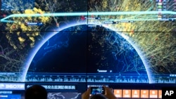 资料照 - 2016年8月16日在北京召开的第四届中国网络安全会议上，一位与会者正在用手机对全球网络攻击检测防御系统的视觉画面拍照。