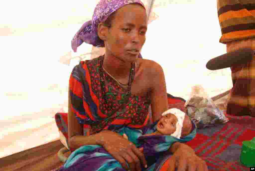 A woman comforts her child, who is suffering from numerous ailments at Hilaweyn Camp. VOA - P. Heinlein