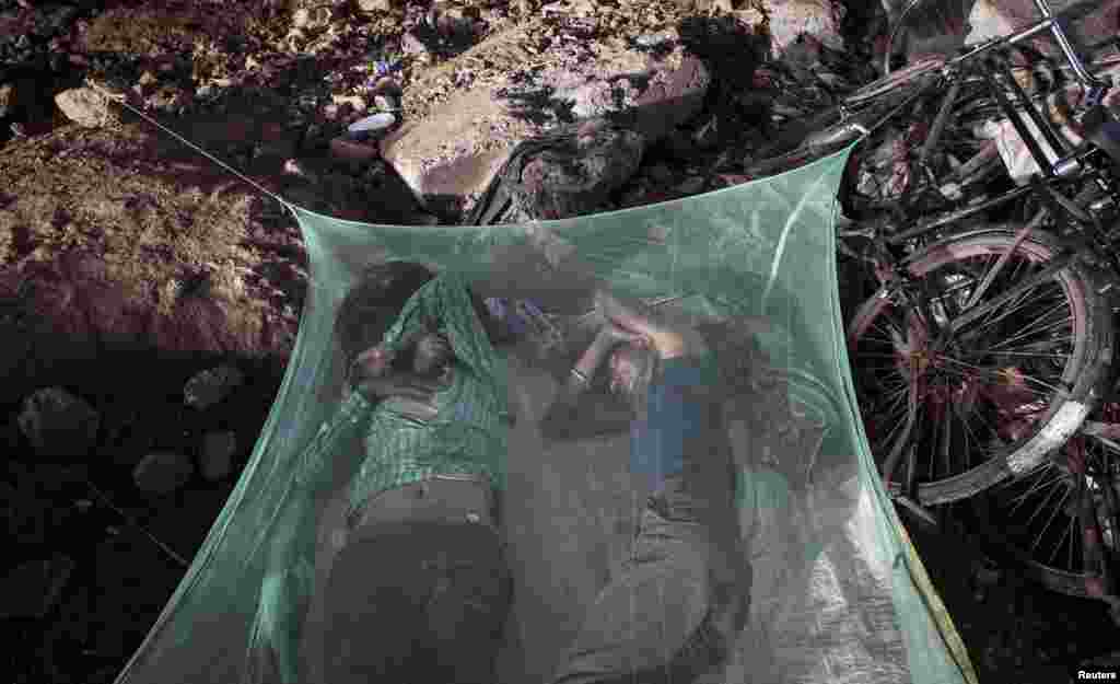Dua pekerja tidur di bawah kelambu pelindung nyamuk di Mumbai, India.