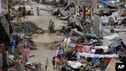 Survivors of Typhoon Haiyan walk amid ruins of their homes in Maraboth, Philippines, Thursday, Nov. 14, 2013. Typhoon Haiyan, one of the most powerful storms on record, hit the country's eastern seaboard on Friday, destroying tens of thousands of building